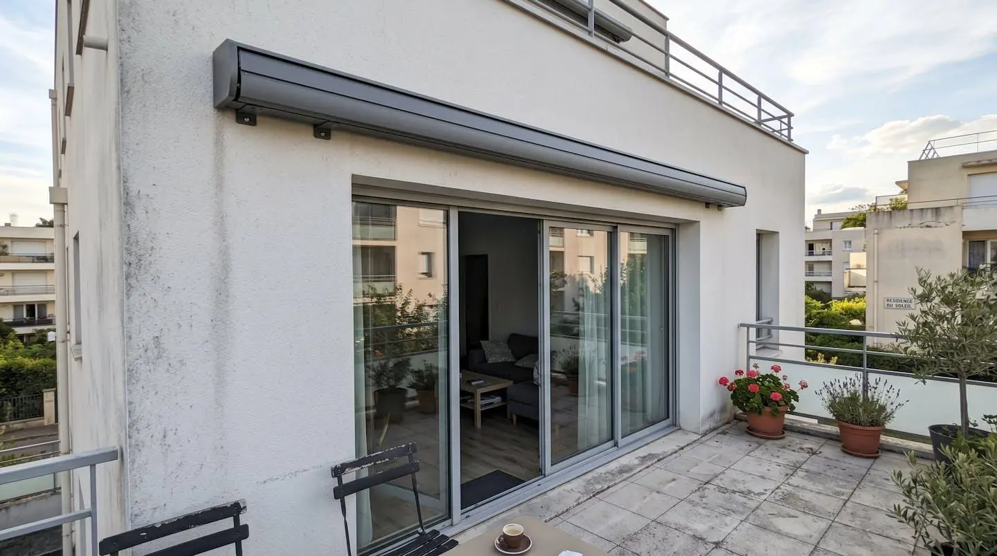 Terrasse française contemporaine avec store banne en position fermée, coffre intégral visible sur façade blanche