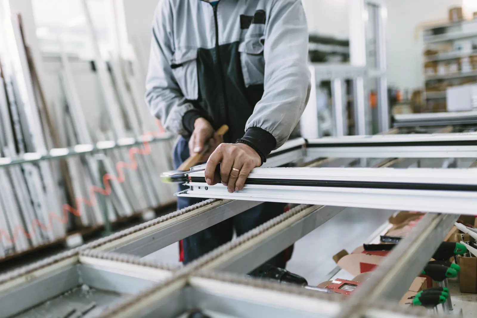 Un artisan prend les mesures d'un cadre de protection solaire sur un établi d'atelier.